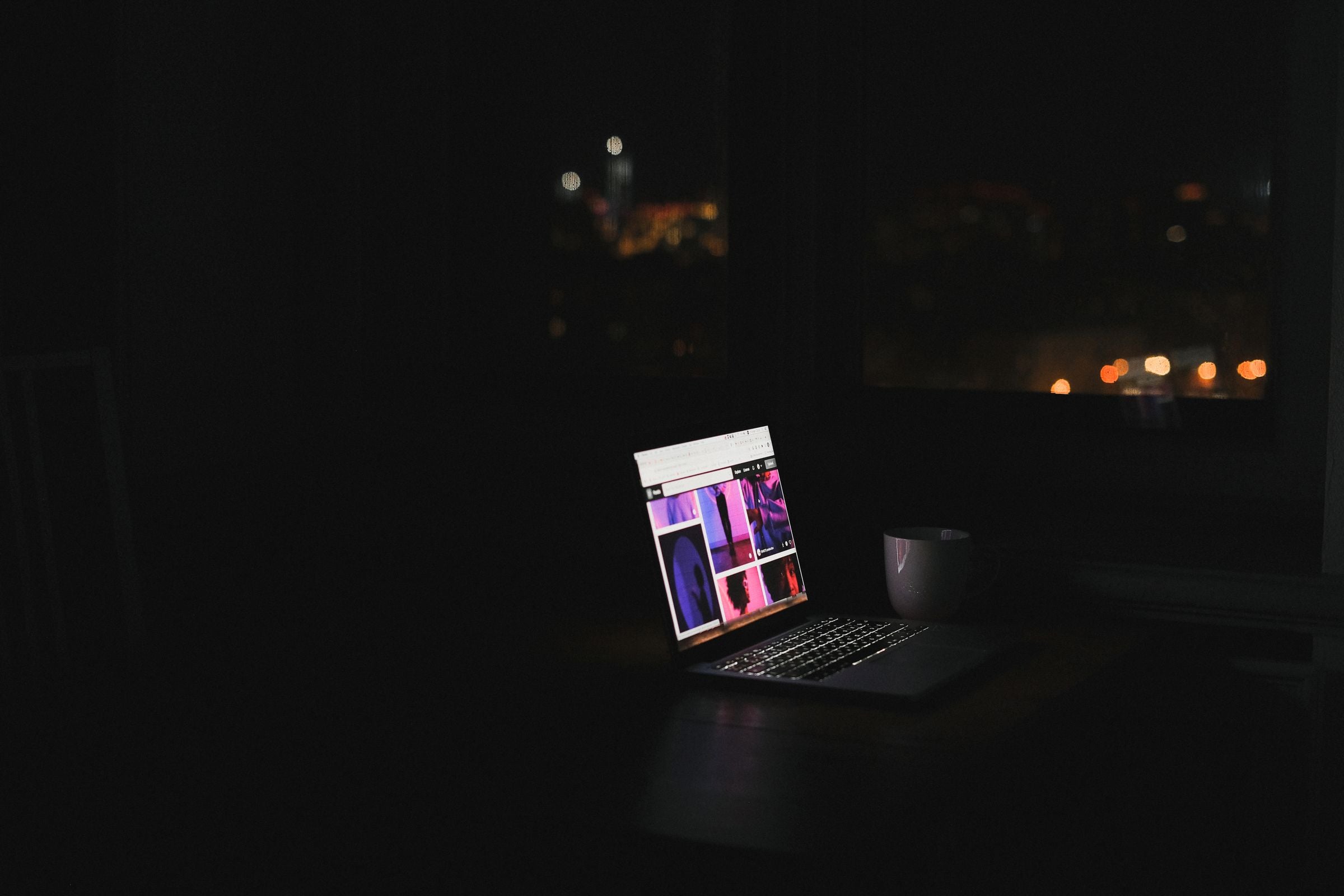 Laptop glowing in a dark room at night with a city skyline — Soch Online Academy hero